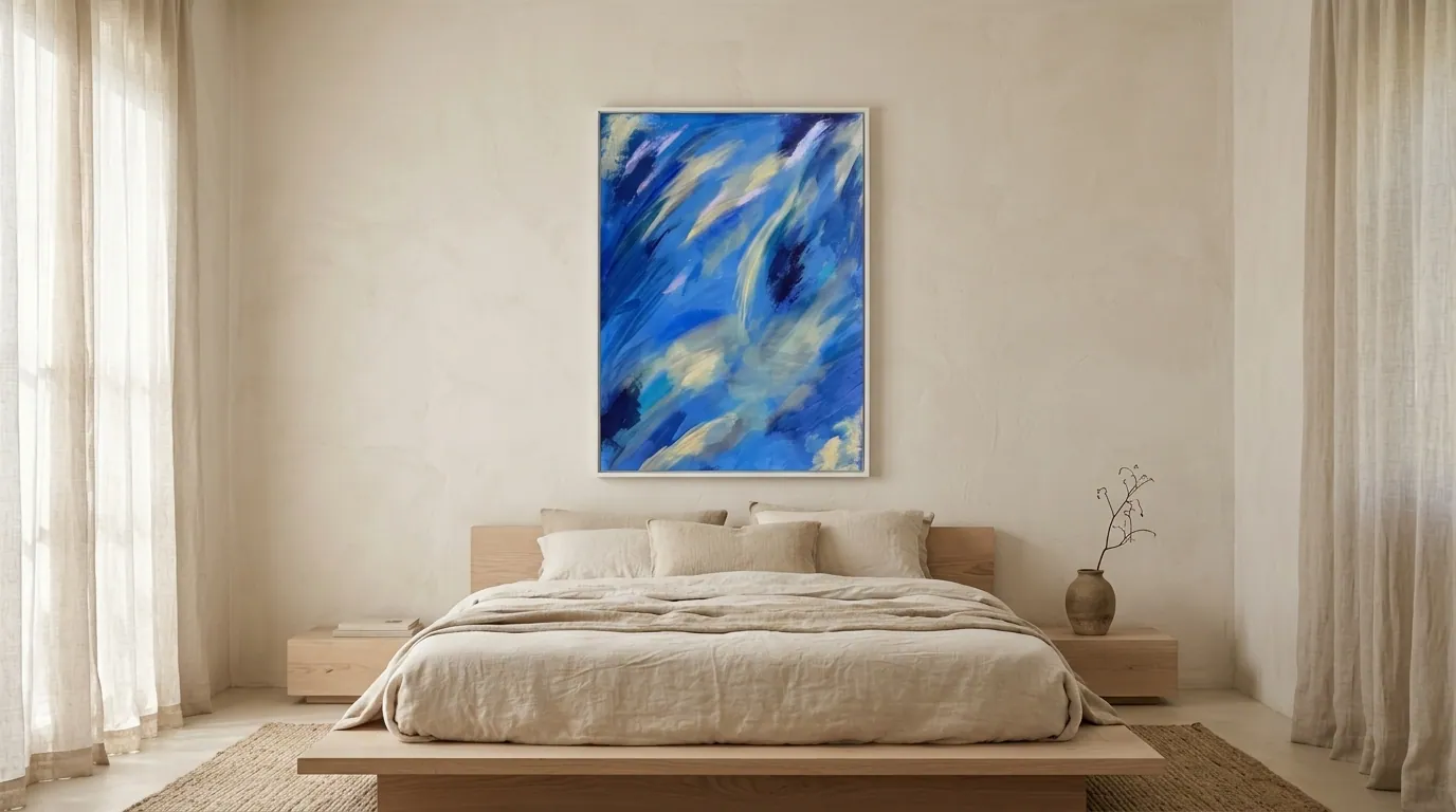 Celestial Drift (70 x 100 cm), Acryl auf Leinwand, Hochformat mit diagonalen Strömungen in Blau, Elfenbein und Indigo mit weißem Rahmen, über einem niedrigen Bett aus hellem Holz mit Leinenbettwäsche zwischen hohen Vorhängen — Alyne Perfeito, Perfeito Studio